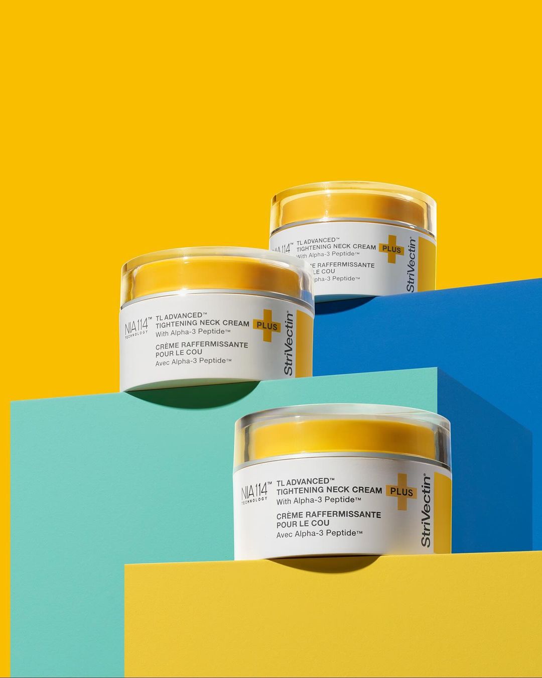 Three jars of StriVectin TL Advanced Tightening Neck Cream PLUS are stacked on geometric platforms against a yellow background.