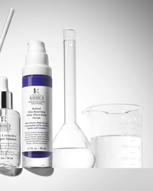 Kiehl's skincare products displayed in a laboratory-like setting, including retinol serum and spot solution bottles next to beakers.