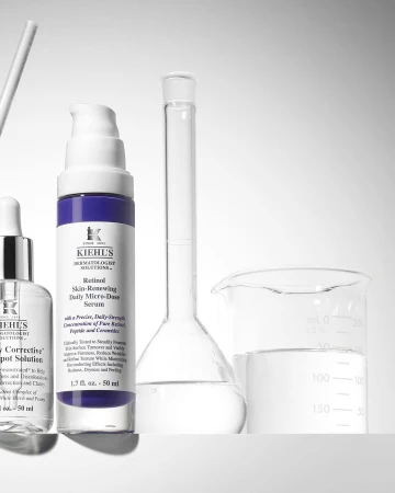 Kiehl's skincare products displayed in a laboratory-like setting, including retinol serum and spot solution bottles next to beakers.