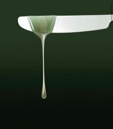 Close-up of a white butter knife dripping viscous green liquid against a dark background
