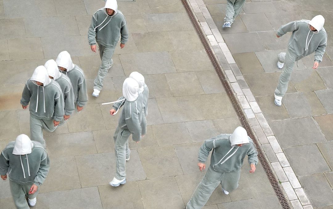 High-angle view of multiple adult males wearing matching grey hooded tracksuits walking on stone tiles, creating a unique urban fashion scene.