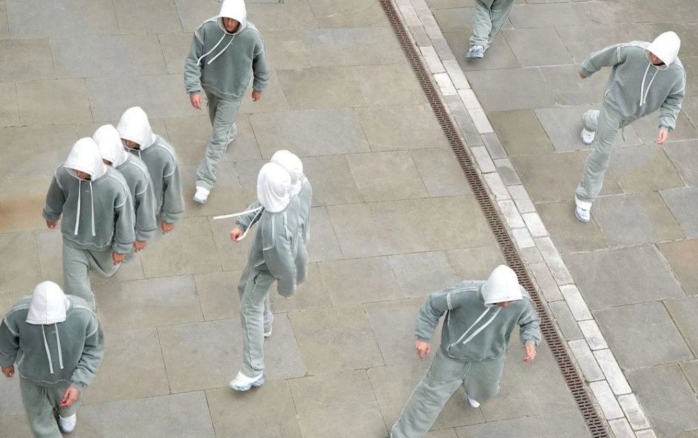 High-angle view of multiple adult males wearing matching grey hooded tracksuits walking on stone tiles, creating a unique urban fashion scene.