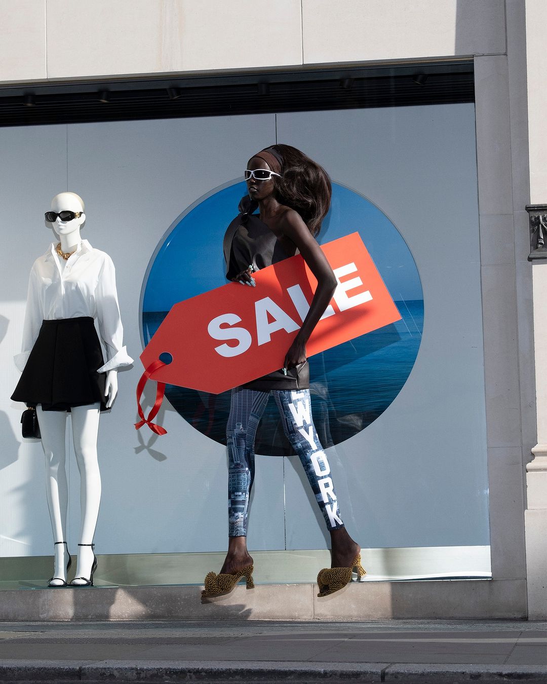 Fashion shoot: Model wearing New York leggings in a store window display with a mannequin and a 'SALE' sign.
