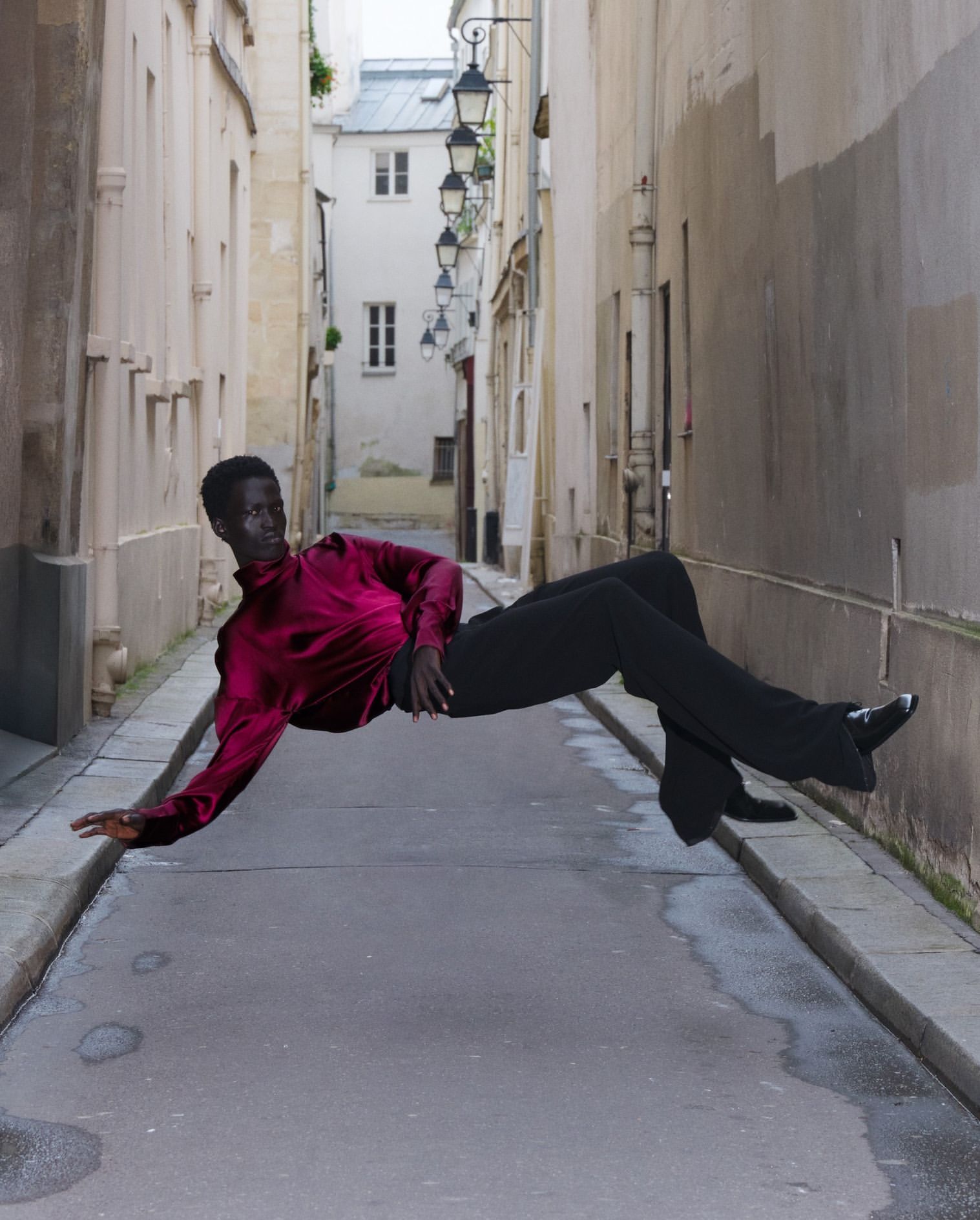 Person in magenta blouse and black pants appears to be floating above cobblestone street in alley, Paris.