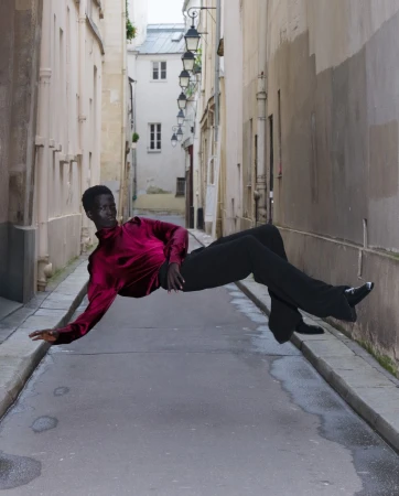 Person in magenta blouse and black pants appears to be floating above cobblestone street in alley, Paris.