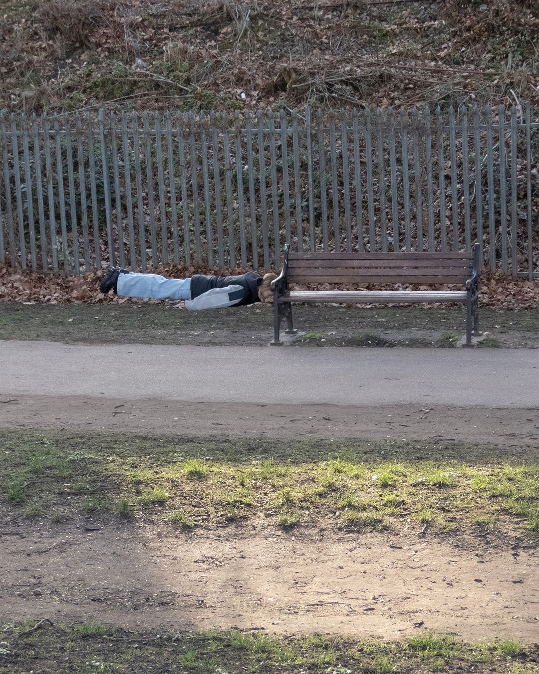 Person suspended horizontally in mid-air holding onto a wooden park bench in an outdoor park setting.
