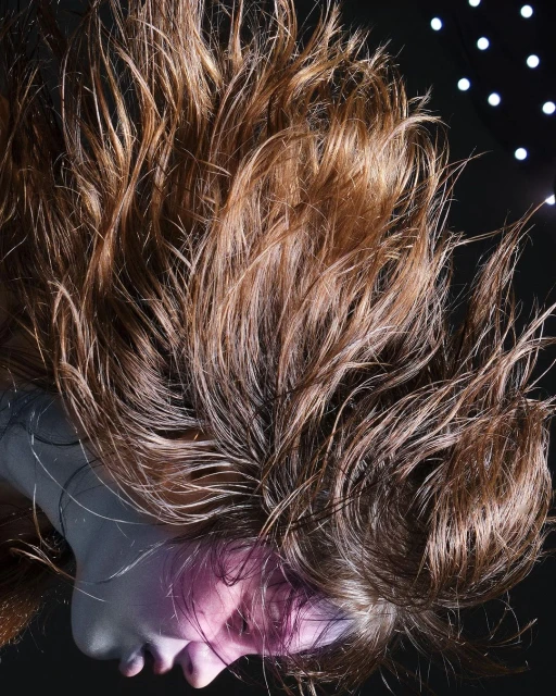 Dramatic portrait of a woman with wet, tousled brown hair against a dark background with bokeh lights, showcasing beauty and texture.