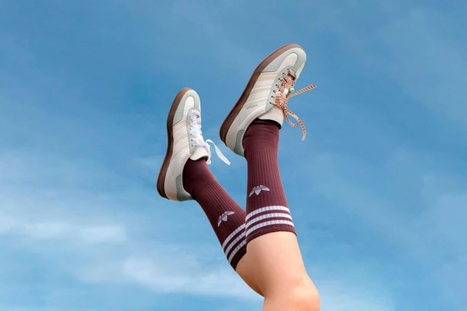 Legs raised against a clear blue sky wearing cream sneakers with patterned laces and burgundy crew socks with white stripes.