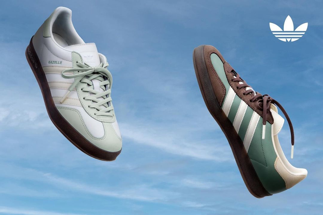 Two Adidas Gazelle sneakers float in a blue sky. One is white with green accents; the other is brown with white accents.