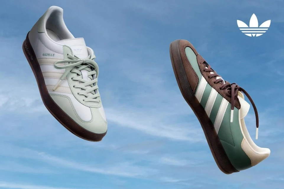 Two Adidas Gazelle sneakers float in a blue sky. One is white with green accents; the other is brown with white accents.