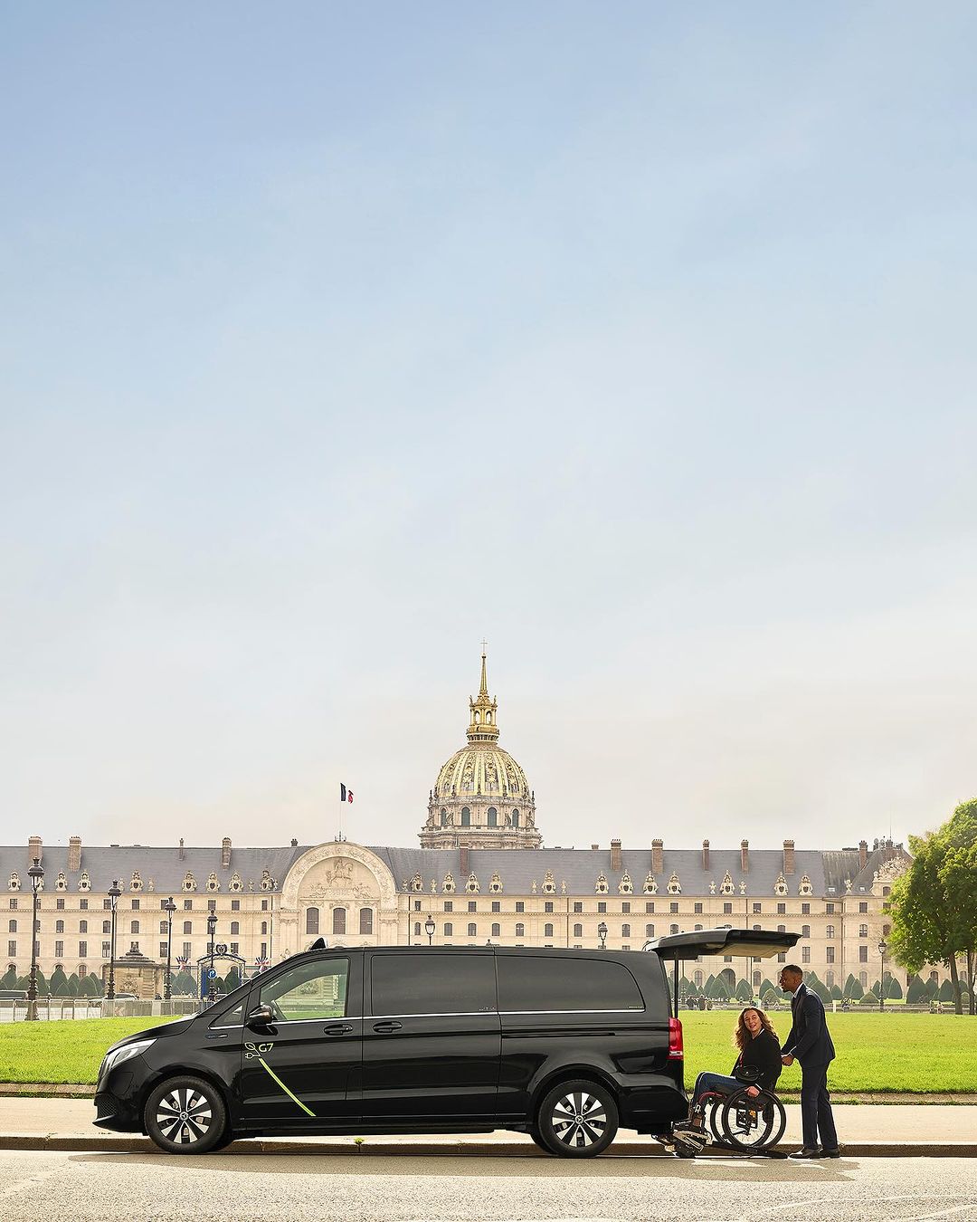 Black van with wheelchair ramp extended on a city street. A woman sits in the wheelchair and a man in a suit assists.