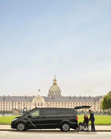 Black van with wheelchair ramp extended on a city street. A woman sits in the wheelchair and a man in a suit assists.