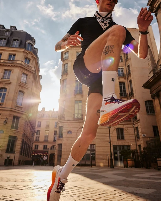 Athletic man running in city street wearing black shorts, t-shirt, bandana and running shoes with sun flare, urban setting and architecture.
