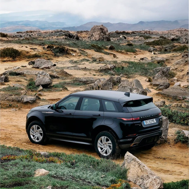 Black Range Rover Evoque SUV on a rocky road, showcasing automotive design and off-road capability with a mountain backdrop on an overcast day.