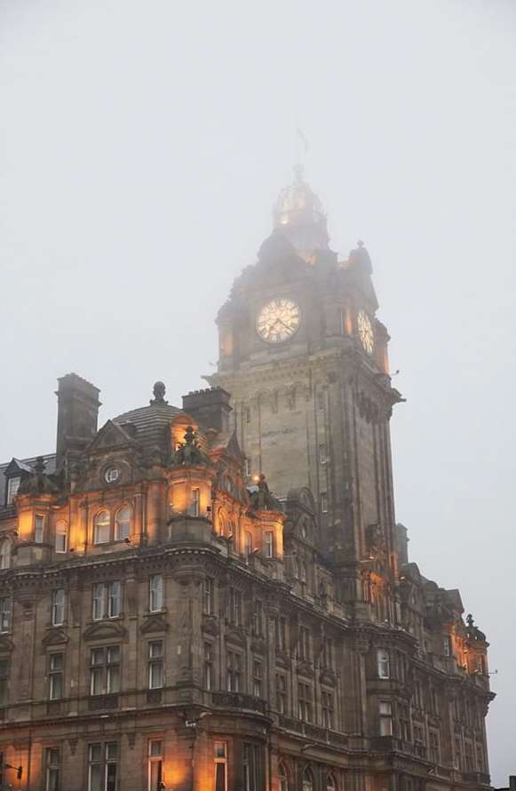 Architectural shot of the Balmoral Hotel clock tower in Edinburgh, Scotland, viewed from a low angle during a foggy day.