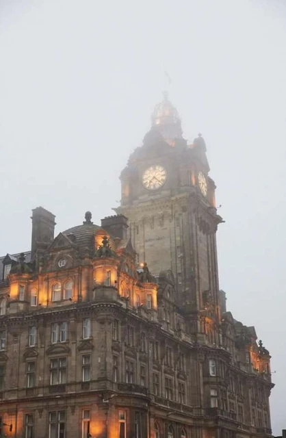 Architectural shot of the Balmoral Hotel clock tower in Edinburgh, Scotland, viewed from a low angle during a foggy day.