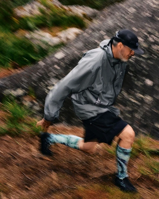 Mature man in athletic gear runs on a grassy slope in an outdoor setting with a large rock formation in the background, captured with motion blur.
