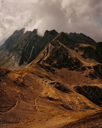 Dramatic mountain peaks under a cloudy sky, showcasing rugged terrain and natural beauty, with a warm, desaturated color palette.