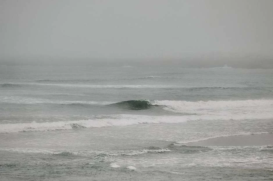 Ocean view with waves under a hazy sky, capturing a serene seascape with a moody atmosphere, showcasing the natural beauty of the coast.