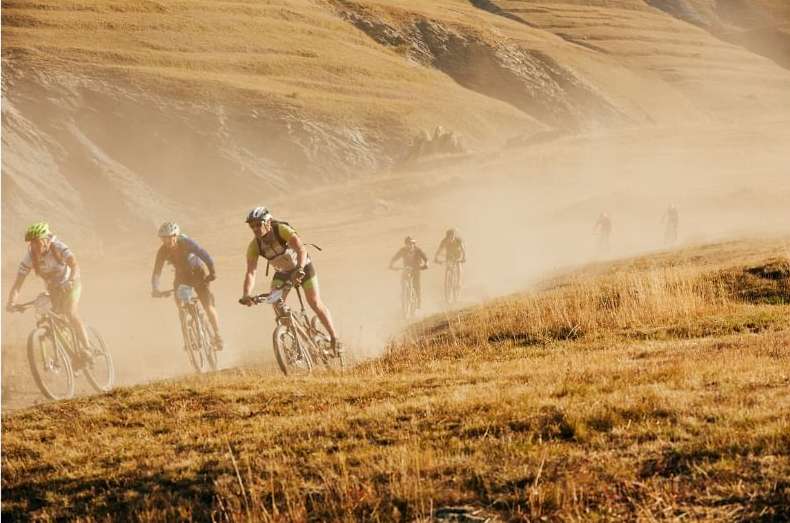 Group of cyclists participating in mountain bike race riding downhill on a dusty trail in a mountain landscape. Outdoor sport event.