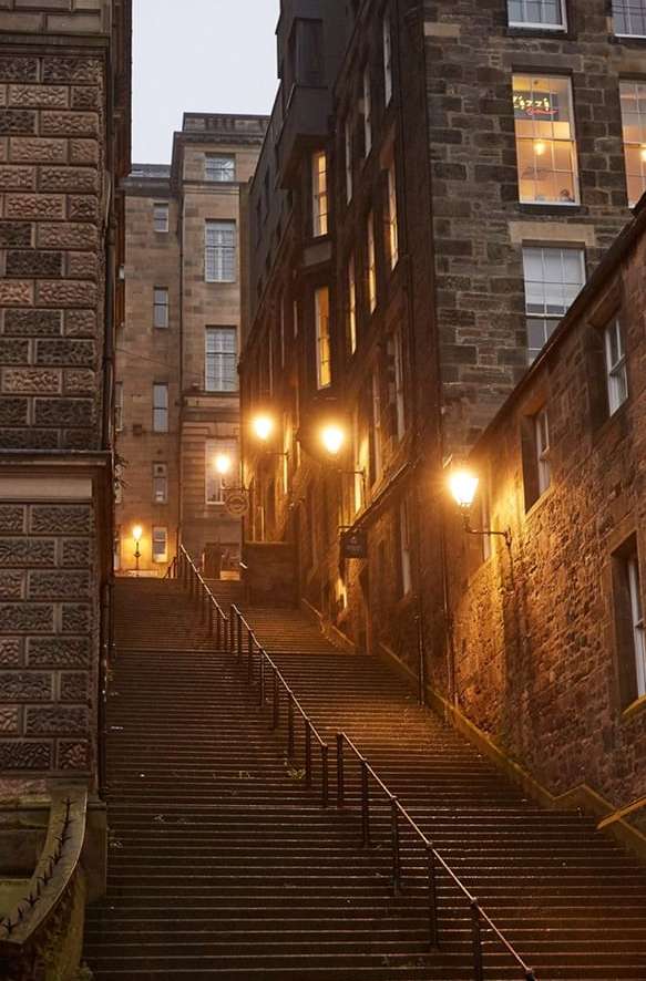 Long staircase ascends between old stone buildings in a nighttime urban scene lit by streetlights, creating a captivating architectural view.