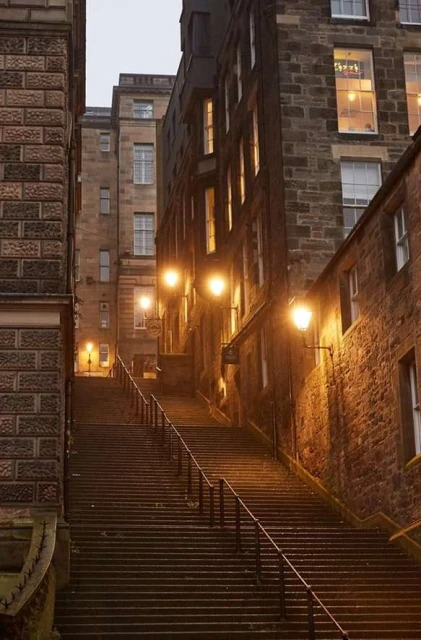 Long staircase ascends between old stone buildings in a nighttime urban scene lit by streetlights, creating a captivating architectural view.