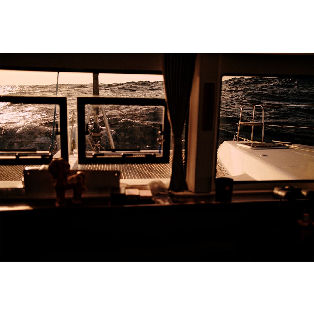 Ocean view from a boat cabin window with rough seas visible through the glass. The white boat deck is seen on the right.