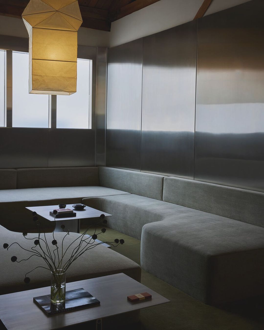 Indoor seating area features an L-shaped sofa and a coffee table with a modern lamp and neutral tones in a minimalist space.