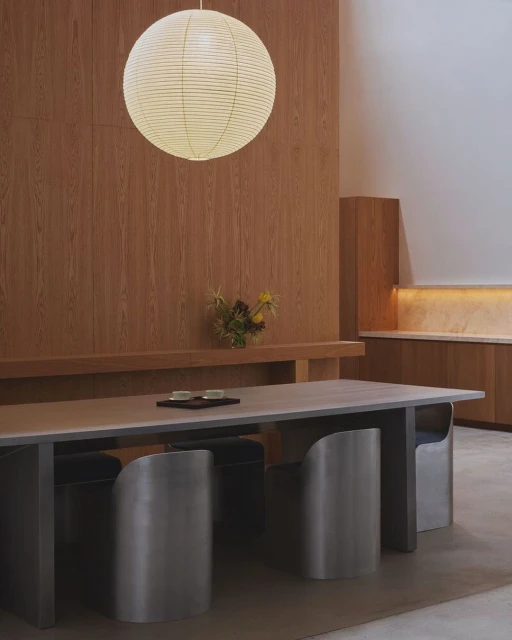 Minimalist dining room featuring a light wood table with metal chairs, a paper lantern pendant light, and light wood wall paneling.