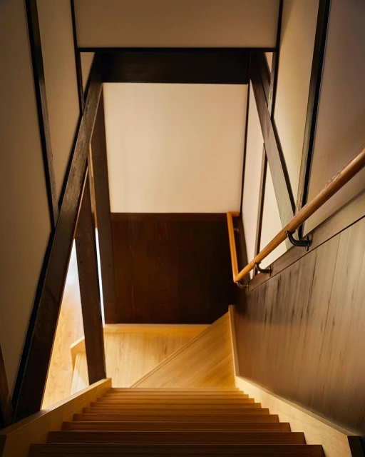 Interior shot of a wooden staircase with brown wood trim, white walls, and a light wood floor, capturing architectural details.