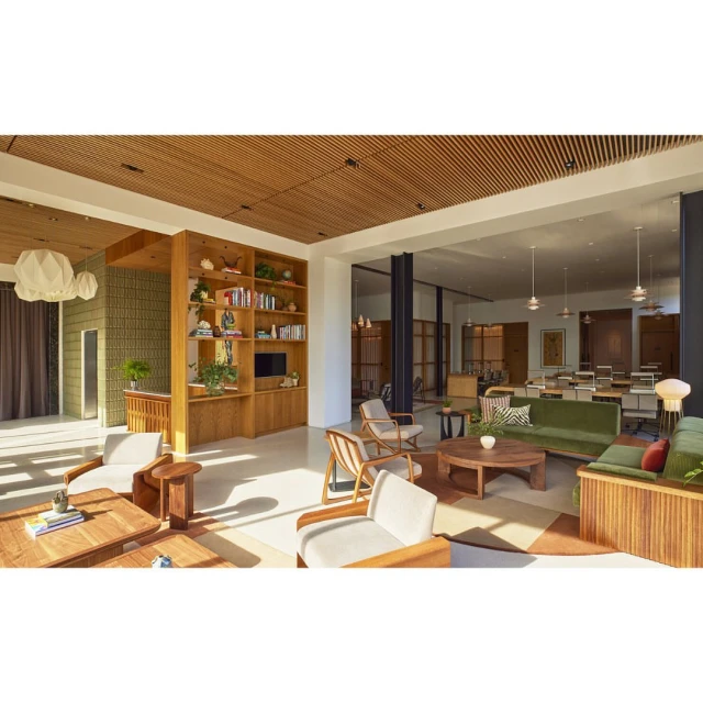 Bright, sunlit hotel lobby and co-working space with lounge furniture, wooden shelving, and desks under pendant lights in the background.