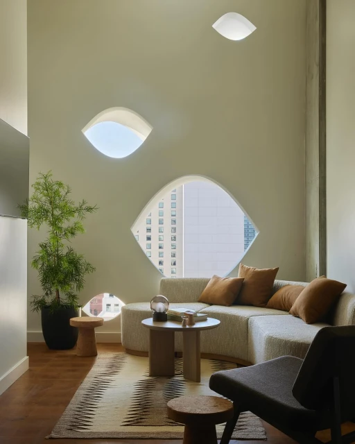 Indoor living space with a curved sofa, accent tables, and geometric windows, complemented by neutral tones and natural light.