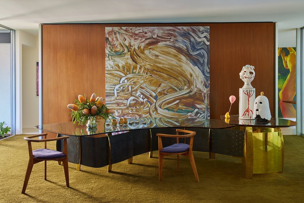 Modern home interior featuring a desk with unique art pieces and decorative vases, complemented by wooden chairs and olive green carpet.