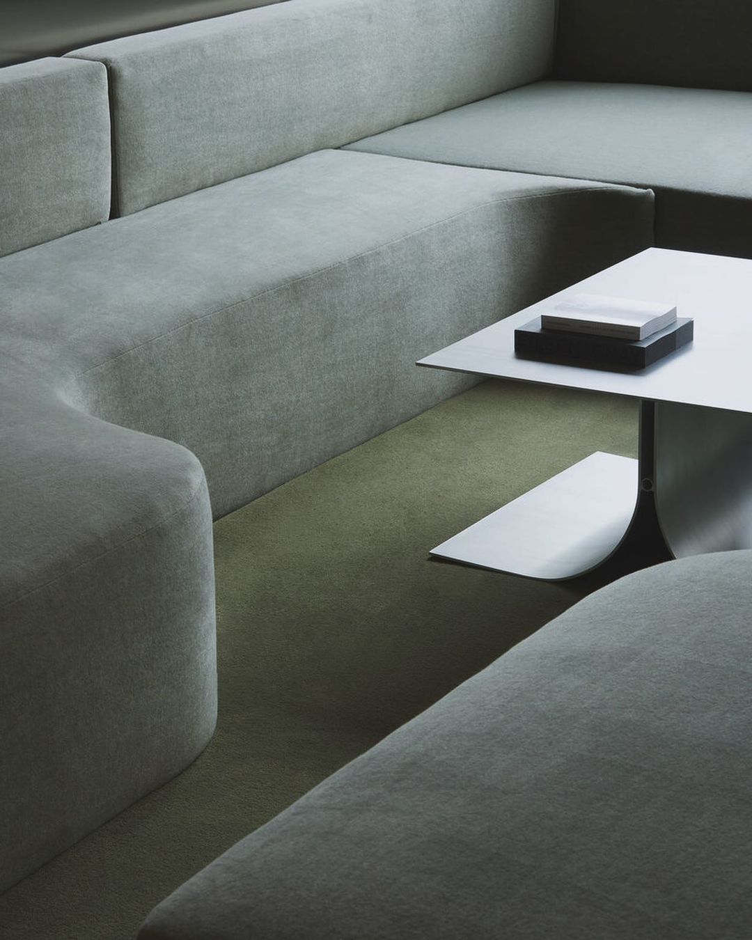 Interior view of a sectional sofa in a neutral color, complemented by a square white table with a black base, creating a minimalist aesthetic.