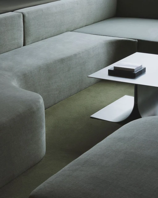 Interior view of a sectional sofa in a neutral color, complemented by a square white table with a black base, creating a minimalist aesthetic.