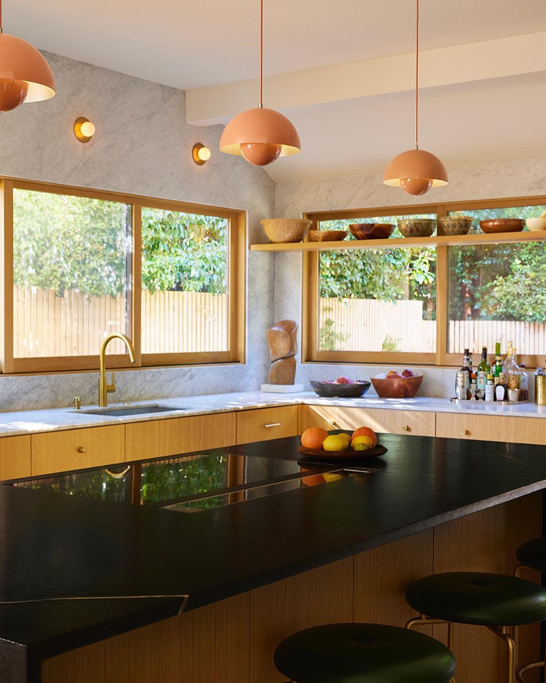 Bright, modern kitchen with black countertops, wooden cabinets, and a view to the backyard; mushroom-shaped pendant lights overhead.