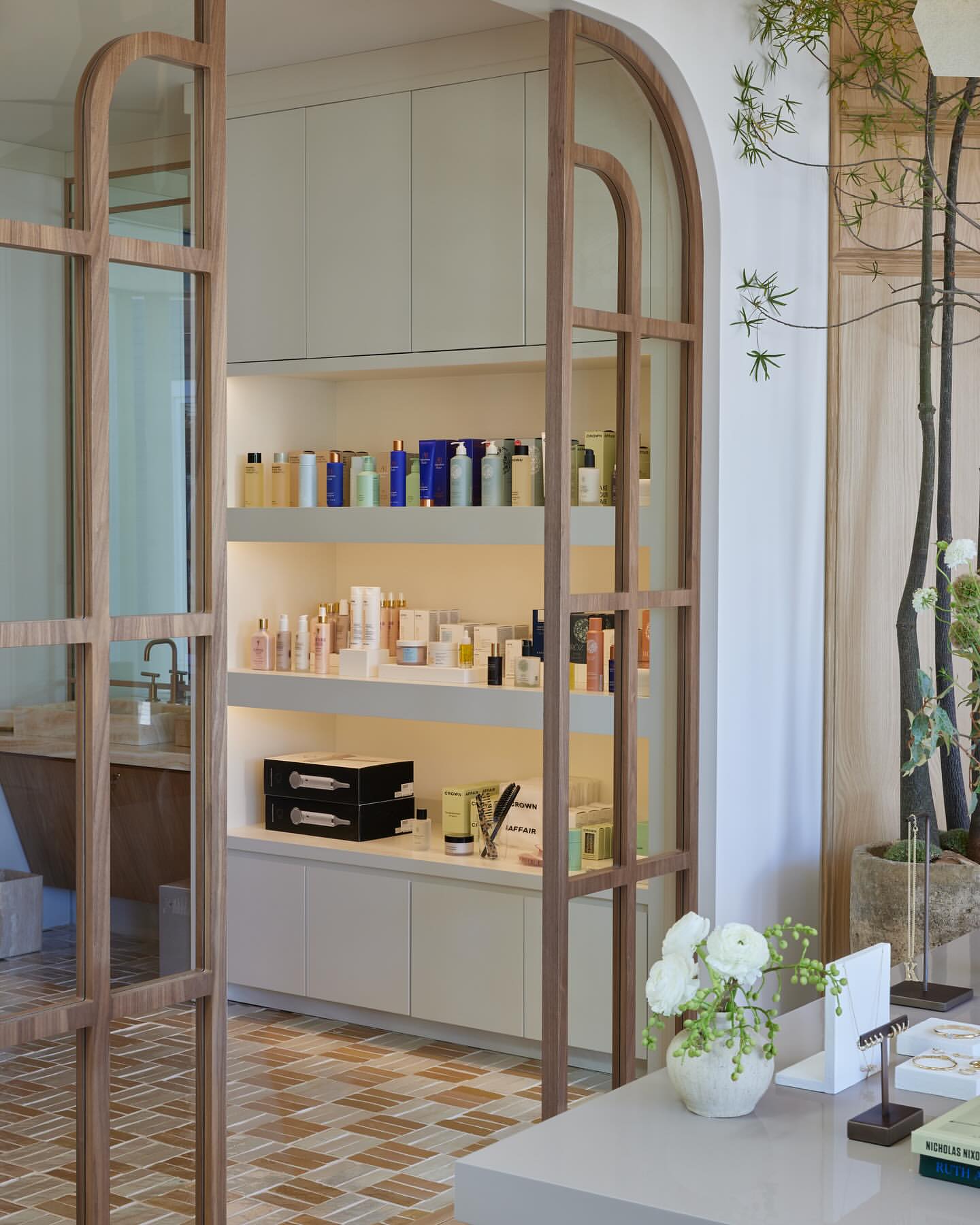 Bright, upscale retail interior featuring beauty and wellness products displayed on illuminated shelving, with natural light and chic decor.