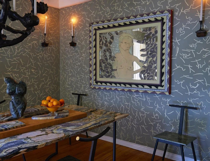 Interior view of dining room with marble table, black chairs, a black chandelier, and framed artwork on a patterned olive-green wall.