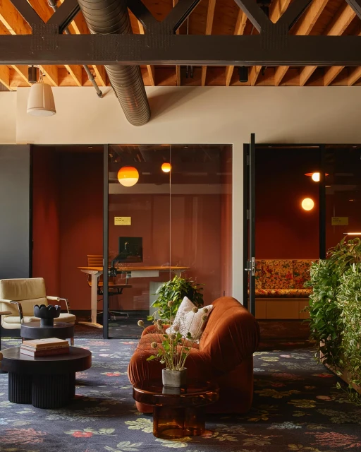 Interior view of an office lounge area with a floral patterned rug, comfortable seating, and plants adding a touch of nature.