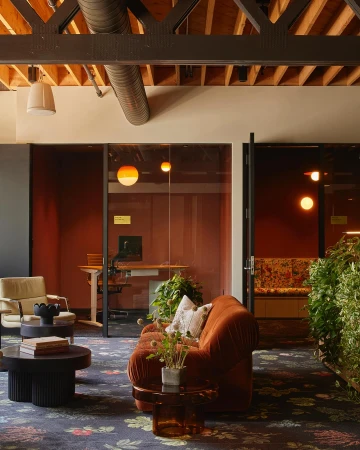 Interior view of an office lounge area with a floral patterned rug, comfortable seating, and plants adding a touch of nature.