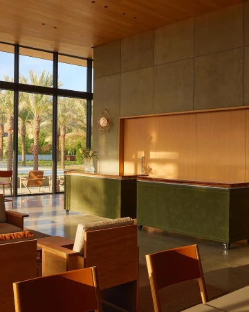 Interior view of a modern building lobby featuring a seating area, reception desks, and large windows showcasing palm trees outside.