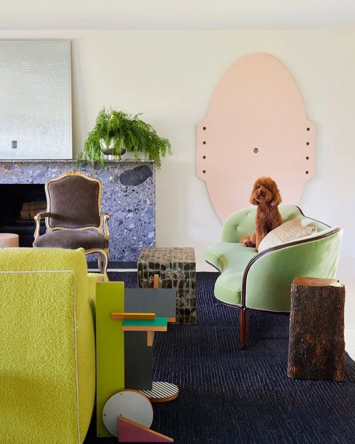 Interior design featuring green and brown tones, accent furniture, stone fireplace, abstract art, and a poodle sitting on a green chair.