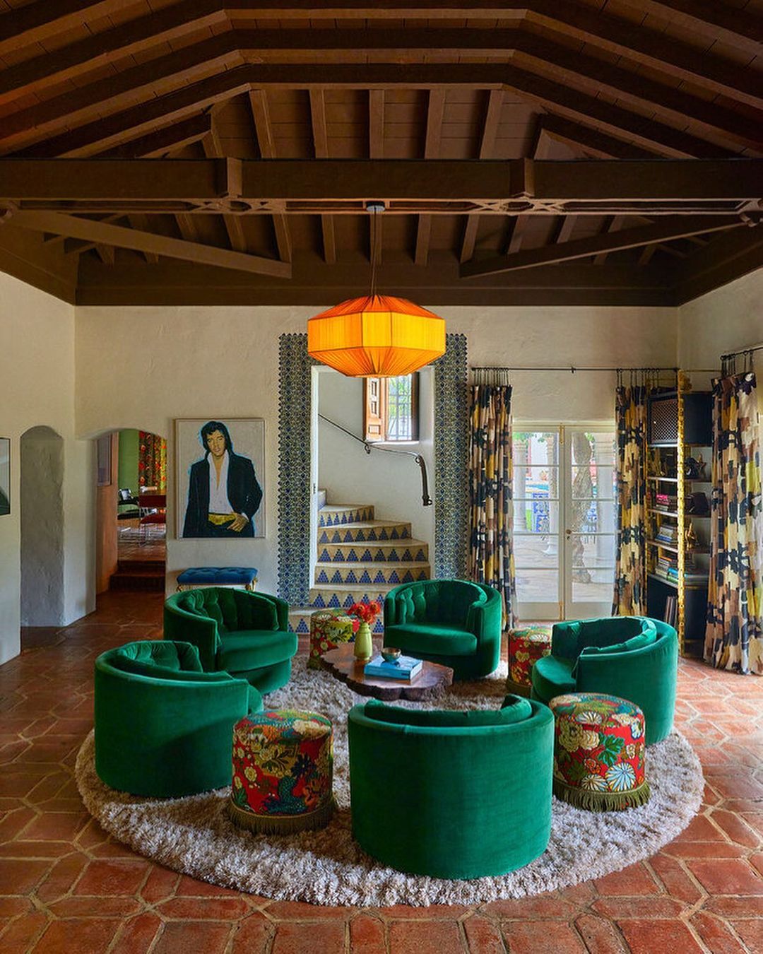 Interior of a living room featuring a round arrangement of green velvet chairs and floral ottomans on a beige shag rug.
