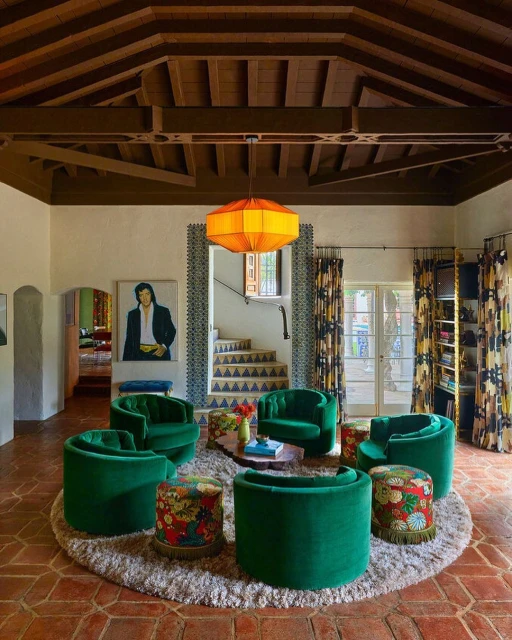Interior of a living room featuring a round arrangement of green velvet chairs and floral ottomans on a beige shag rug.