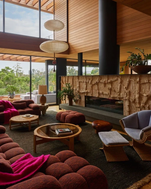 Brown modular sofa and mid-century modern furniture define this living room with a stone fireplace and floor-to-ceiling windows overlooking greenery.