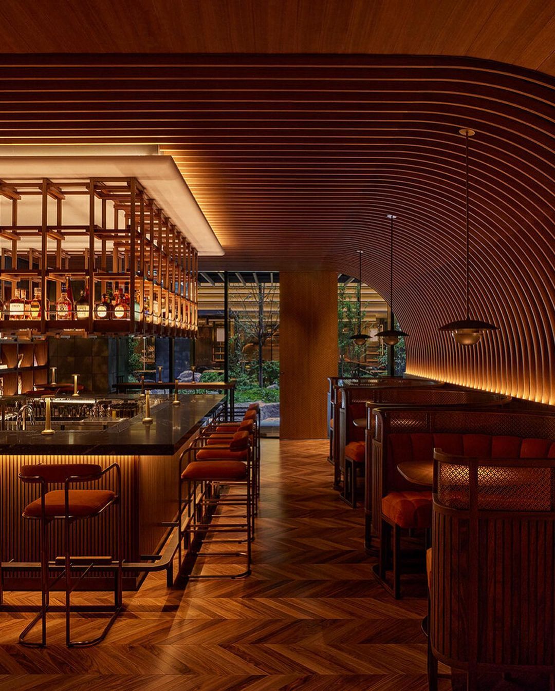 Stylish interior of a bar and restaurant featuring a herringbone wood floor, wooden bar with stools, and booth seating with modern lighting.