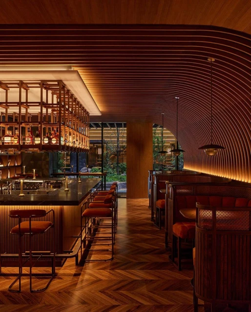 Stylish interior of a bar and restaurant featuring a herringbone wood floor, wooden bar with stools, and booth seating with modern lighting.