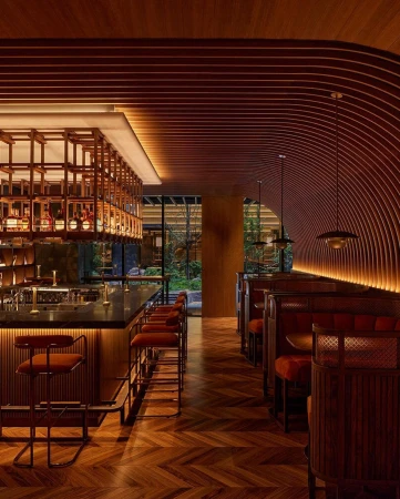 Stylish interior of a bar and restaurant featuring a herringbone wood floor, wooden bar with stools, and booth seating with modern lighting.