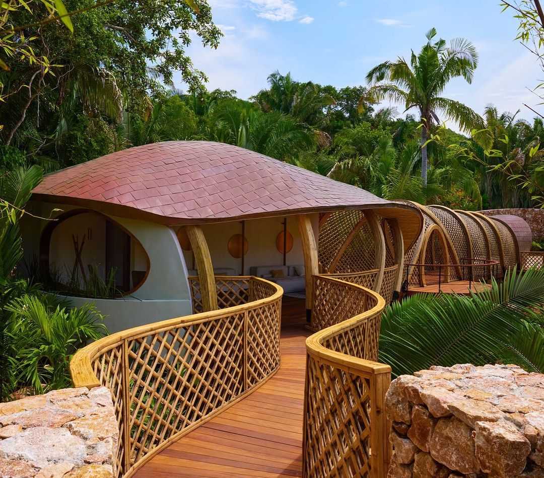 Exterior of tropical villa with wooden walkway, lush green foliage, unique architecture, tile roof, and inviting outdoor living space.