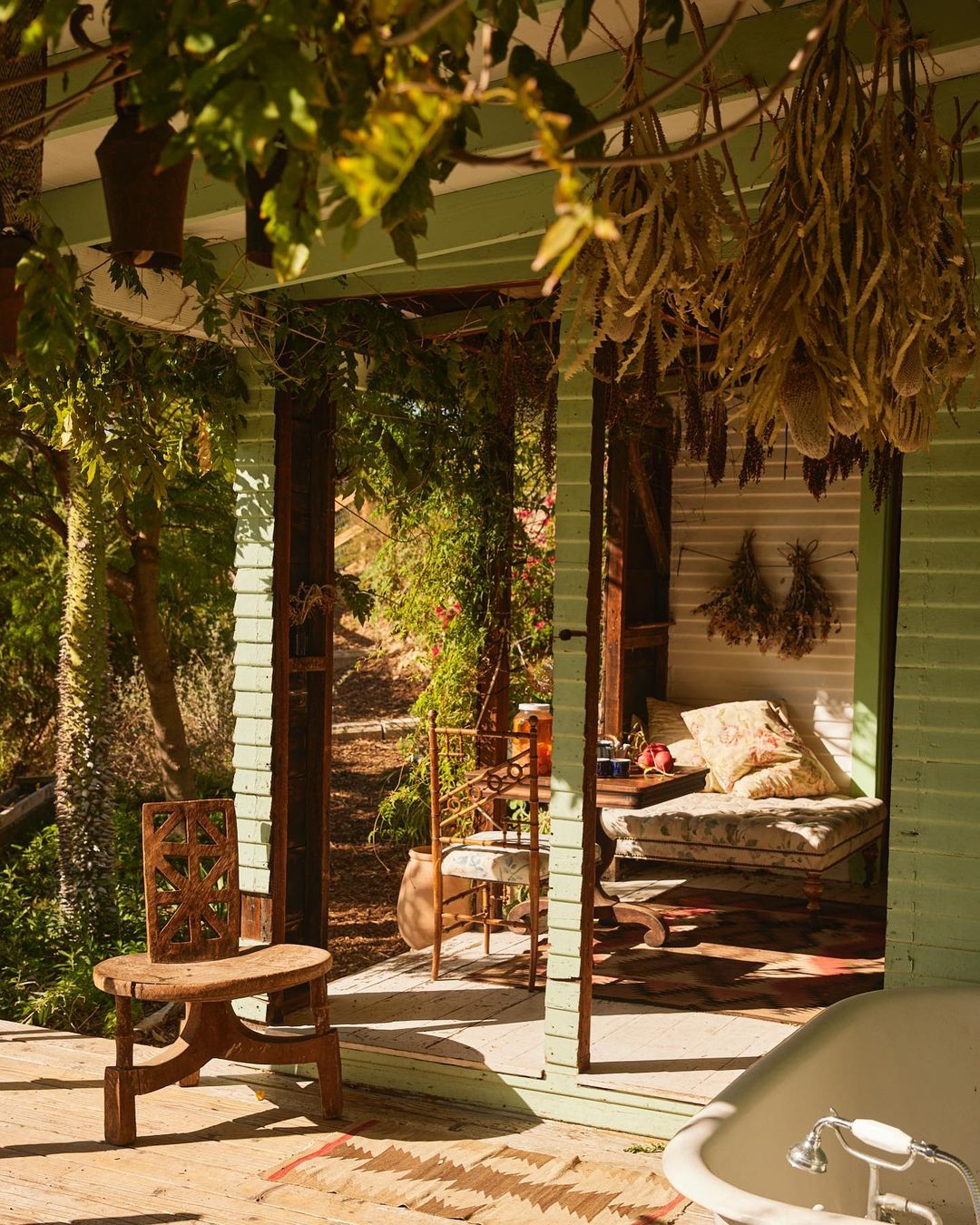 Boho-chic outdoor patio scene featuring a vintage bathtub, wooden chair, and lounge area with decorative plants and natural light.